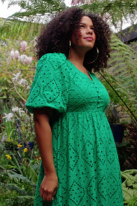 A curly-haired lady wearing a button front green broderie Anglaise midi dress with puff sleeves