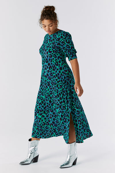 Scamp and Dude Green with Blue and Black Shadow Leopard V-Back Midi Dress | Model with hair in a bun wearing a green dress with black leopard print with heeled silver cowboy boots