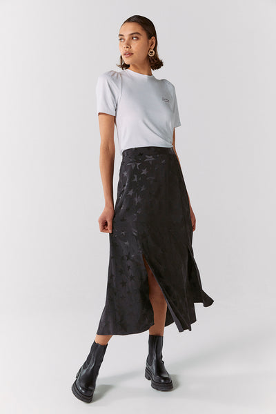 Scamp and Dude Black Jacquard Star Split Front Skirt | Model with short hair looking away from the camera wearing a plain white top with black star printed skirt and black boots