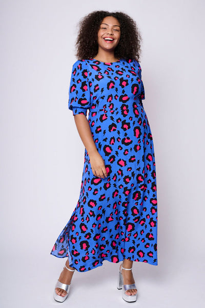 Scamp and Dude Electric Blue with Pink and Black Snow Leopard Midi Dress | Model with curly hair wearing blue and pink leopard print dress with silver high heels