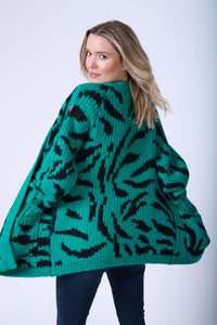 A lady with her hands in the pockets of the teal with black zebra chunky knitted cardigan she is wearing