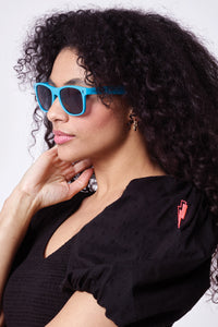 A curly-haired lady wearing neon blue sunglasses with black lightning bolts on the front and smoke coloured lenses