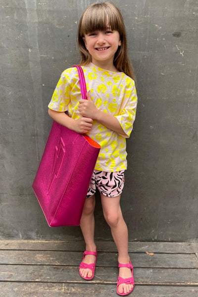 Scamp and Dude | Kids Blush with Neon Yellow Leopard T-Shirt | Young girl wearing a light pink and yellow leopard print top with leopard print shorts holding a pink tote bag