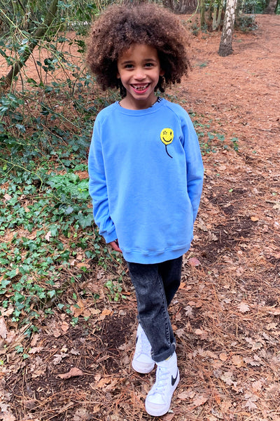 A curly-haired boy wearing a blue sweatshirt with a yellow towelling balloon on the chest
