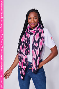 A lady wearing a black with hot pink and pink leopard ikat and lightning bolt print scarf with a black pom pom trim