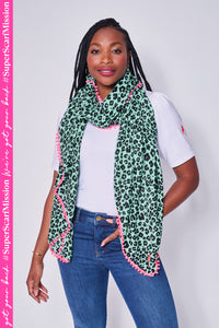 A lady wearing a turquoise with black floral leopard and lightning bolt print scarf with a neon pink pom pom trim