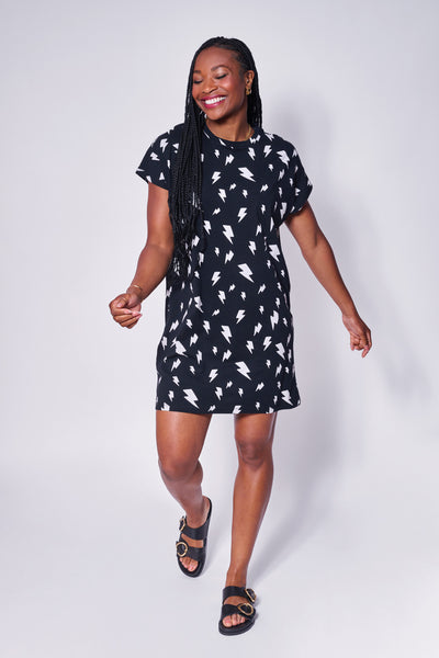 A lady wearing an oversized black with white lightning bolt print T-shirt dress and sandals 