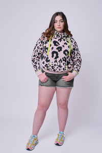 A lady wearing a pale peach with black mixed leopard and lightning bolt cowl neck hoodie with washed grey denim shorts