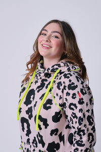 A lady wearing a pale peach with black mixed leopard and lightning bolt cowl neck hoodie with neon yellow details