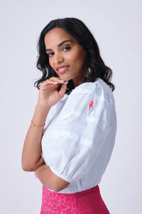 A woman wearing a white T-shirt with pintuck detailing on the sleeves and a neon pink embroidered lightning bolt