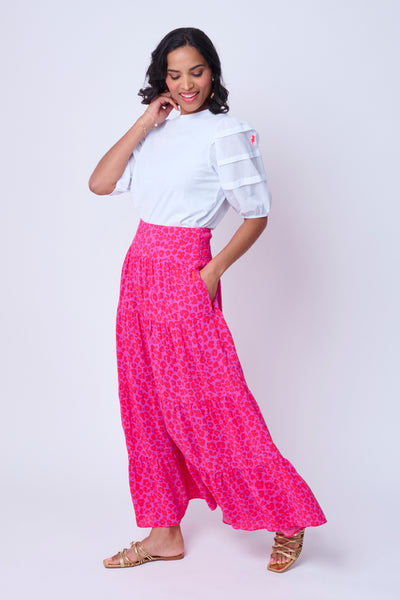A lady wearing a magenta with hot pink floral leopard and lightning bolt print maxi skirt with a white T-shirt tucked in