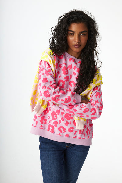 Scamp and Dude Lilac with Neon Pink Leopard Oversized Sweatshirt | Model with curly hair with arms crossed wearing a pink leopard print jumper and blue jeans