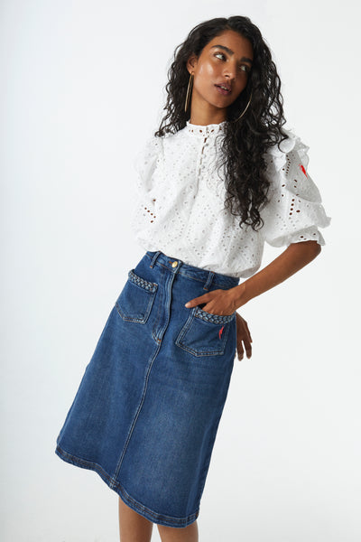 Scamp and Dude Indigo Plait Detail A-Line Denim Skirt | Model with curly hair wearing a white button up blouse and medium wash knee length denim skirt 