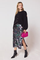 Scamp & Dude Silver with Rainbow Leopard Sequin Split Front Midi Skirt | Model wearing a sequin skirt with a long sleeve black cardigan and pink clutch bag.