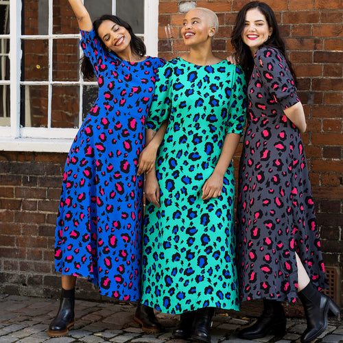 Scamp and Dude | Three women wearing Scamp and Dude leopard print long dresses in pink, blue and green linking arms and smiling at the camera in front of a brick wall