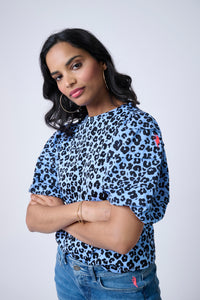 A woman crossing her arms wearing a soft blue with black floral leopard and lightning bolt print pintuck sleeve T-shirt