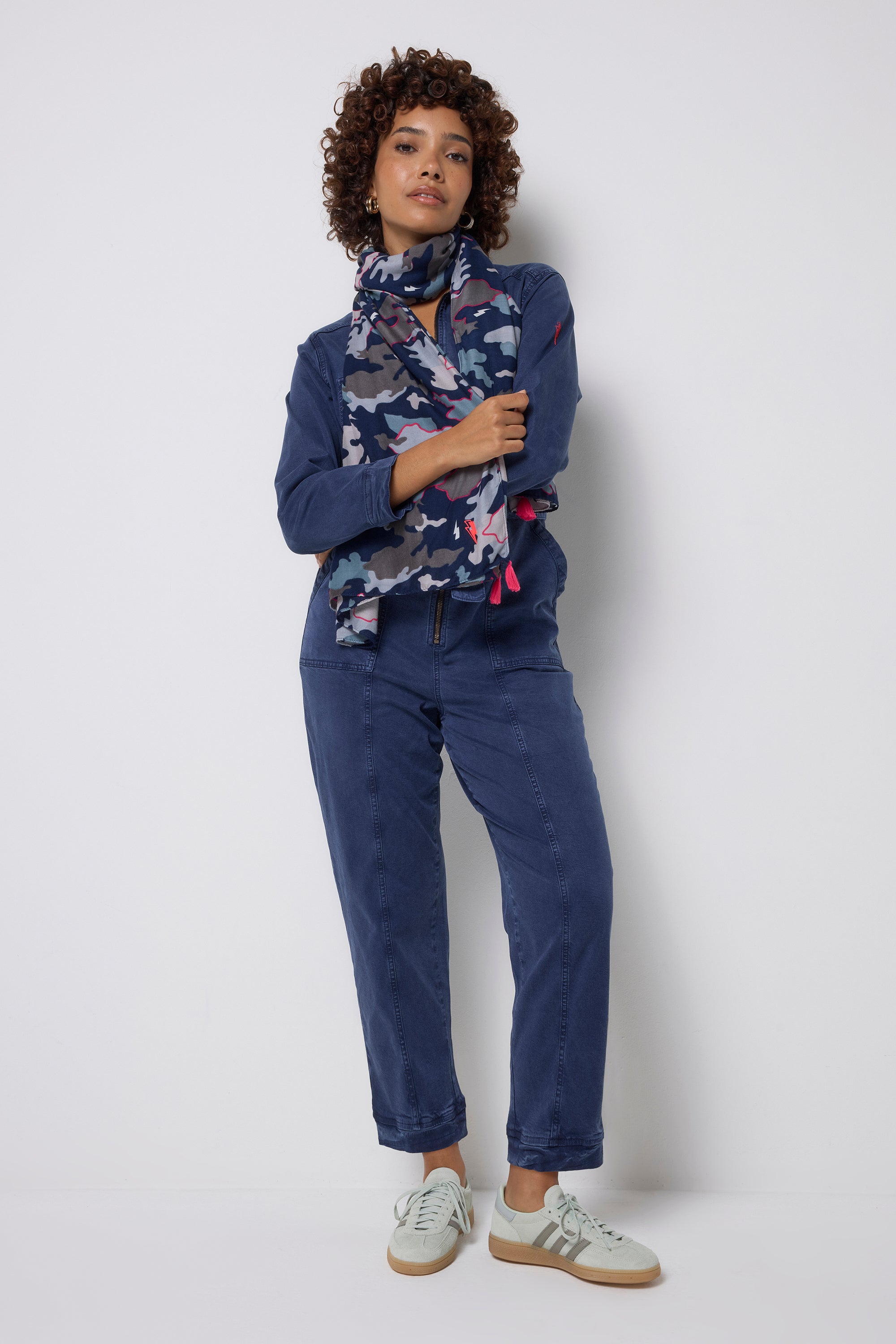 Scamp and Dude Navy with Pink Camo Charity Super Scarf | Model wearing dark blue jumpsuit with a pair of trainers and a camo print super scarf.