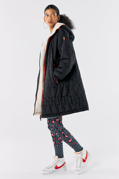 Scamp and Dude Black Reversible Quilted Coat | Model wearing long black quilted coat with leopard print leggings and white trainers
