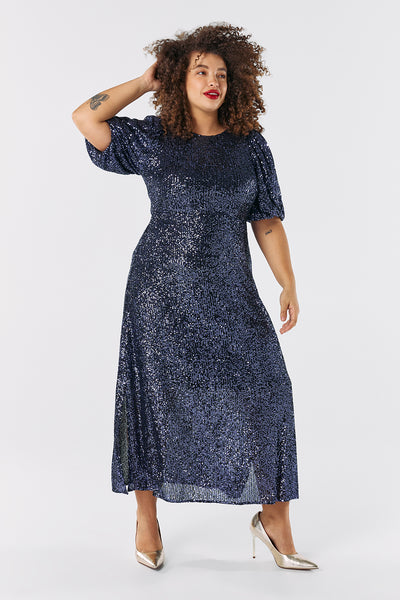 Scamp and Dude Navy Sequin Puff Sleeve Midi Dress | Model with curly hair wearing navy maxi sequin dress with shiny high heels 