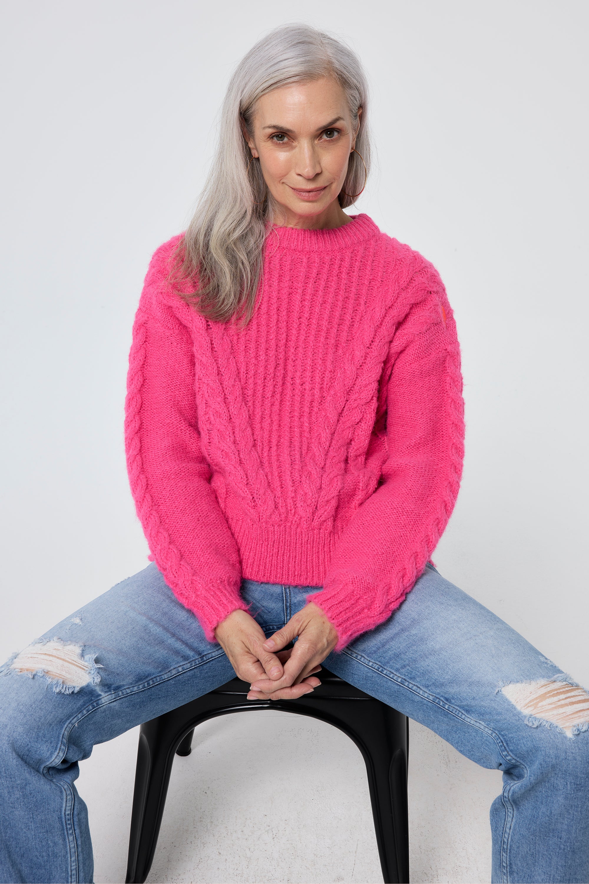 Scamp and Dude Pink Cable Knit Cropped Jumper | Model wearing light blue distressed jeans with a pink cropped knit jumper.