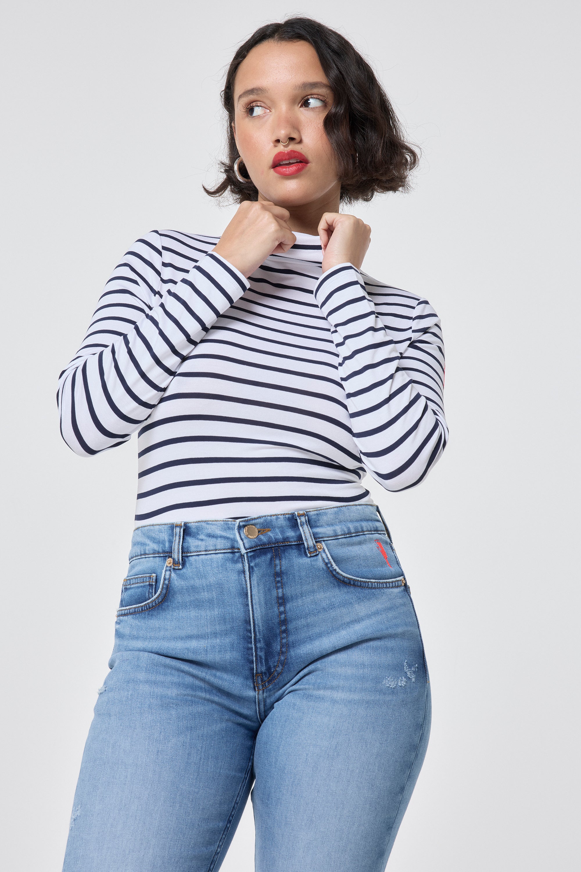 Scamp and Dude Ivory with Navy Stripe Long Sleeve Polo Top | Model wearing an ivory long sleeve high neck top with navy stripes, paired with blue jeans.