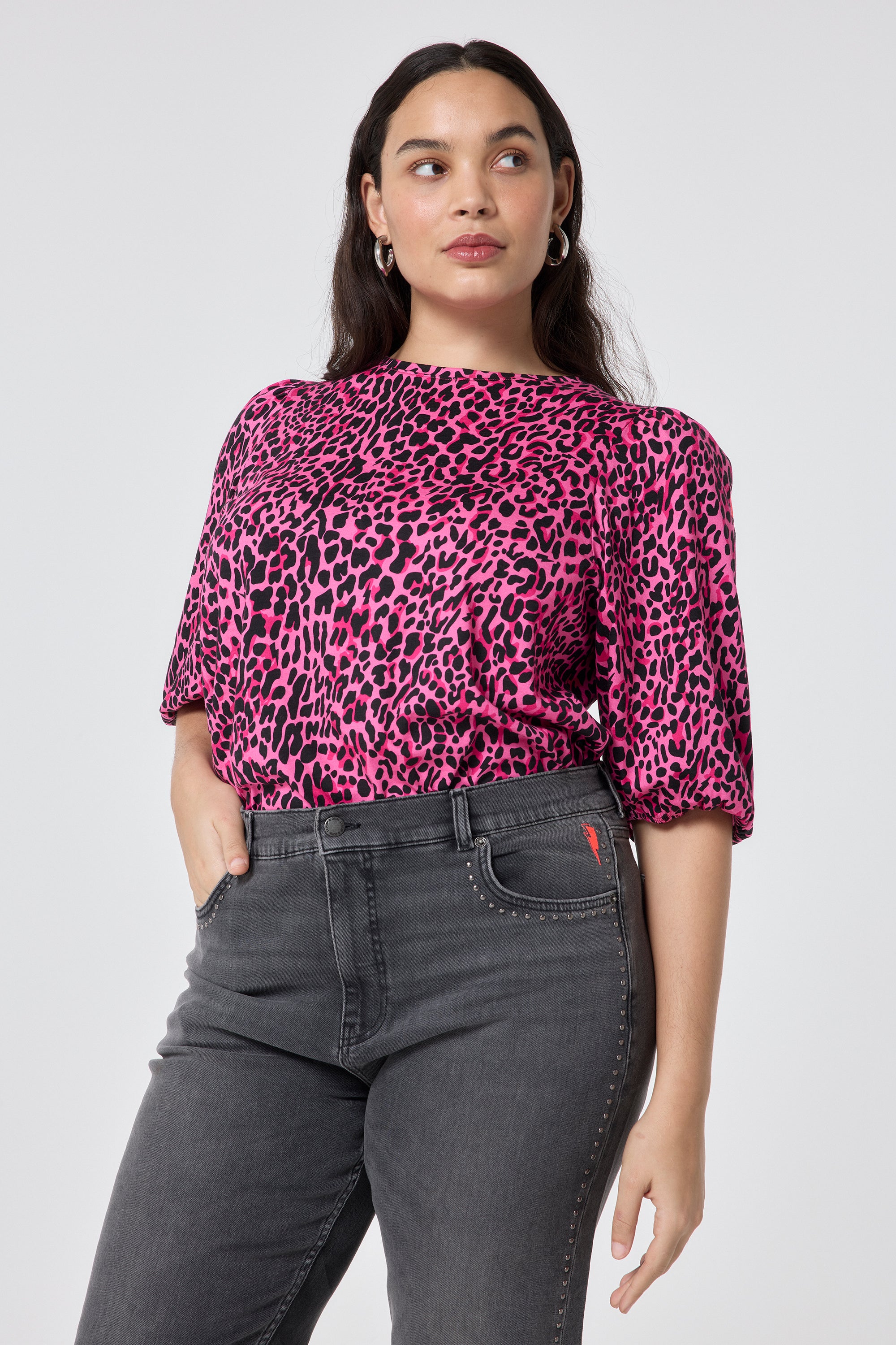 Scamp and Dude Pink with Black Wild Leopard Puff Sleeve T-Shirt | Model wearing a pink t shirt with black leopard print, worn with grey studded jeans.