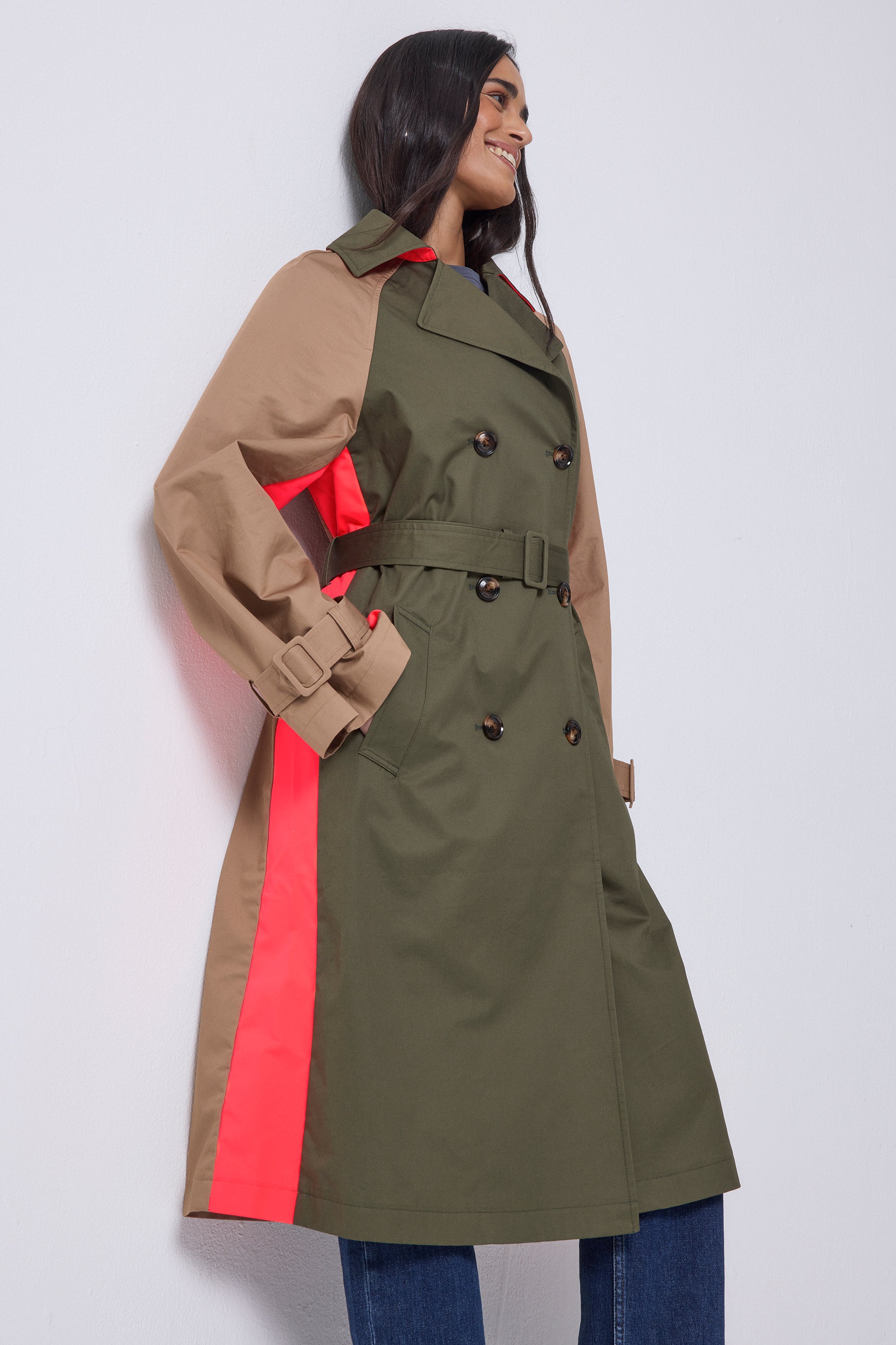 Scamp and Dude Khaki with Camel and Coral Colour Block Trench Coat | Model wearing a khaki trench coat that has camel sleeves and a coral stripe. Paired with blue jeans and heeled boots.