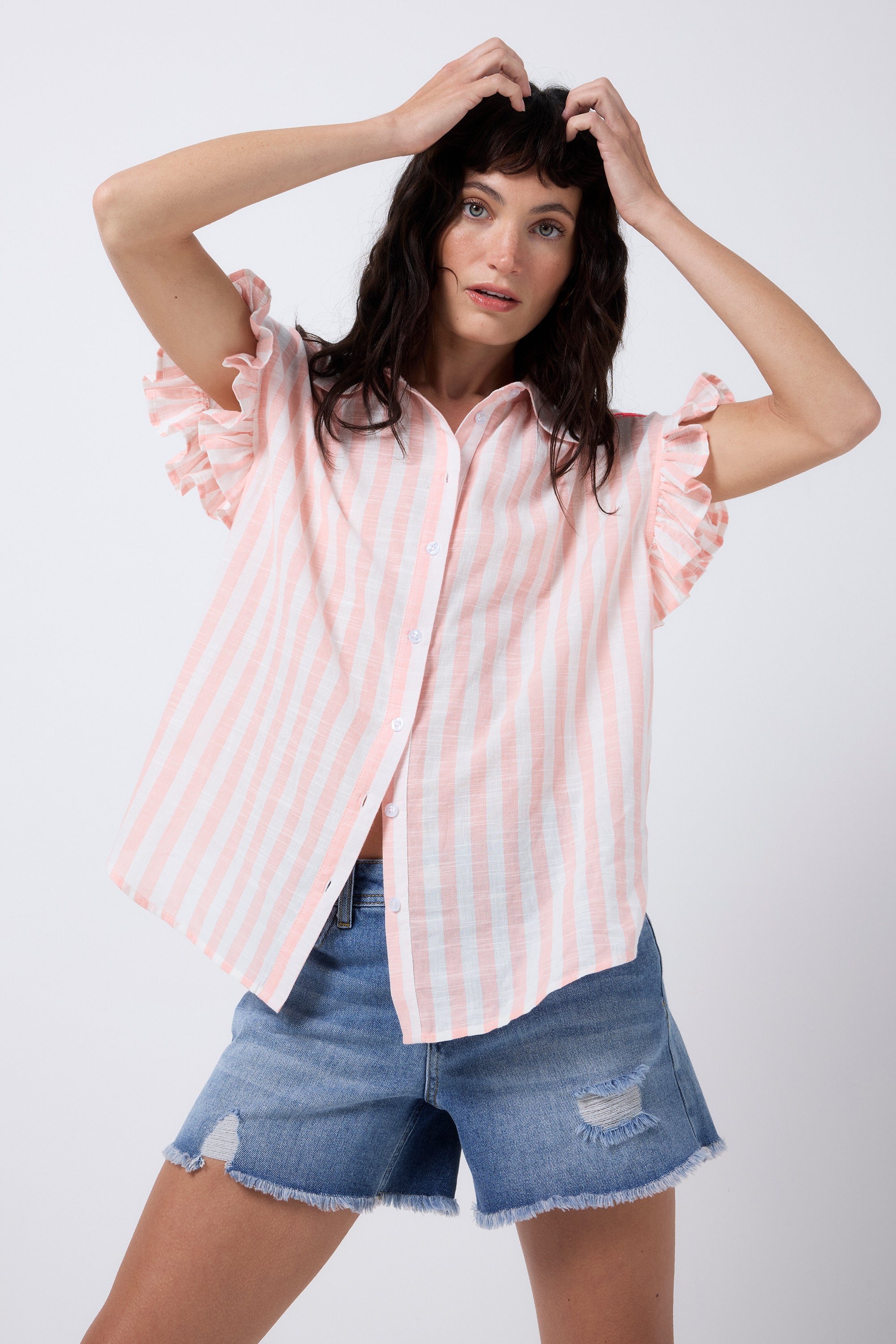 Scamp and Dude Coral and White Stripe Frill Sleeve Shirt | Model wearing a pair of distressed blue denim shorts with a coral and white stripe shirt that has short frill sleeves.