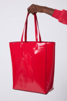 Scamp and Dude Red Patent Lightning Bolt Tote Bag | Model wearing a red sweatshirt, holding a red patent tote bag.