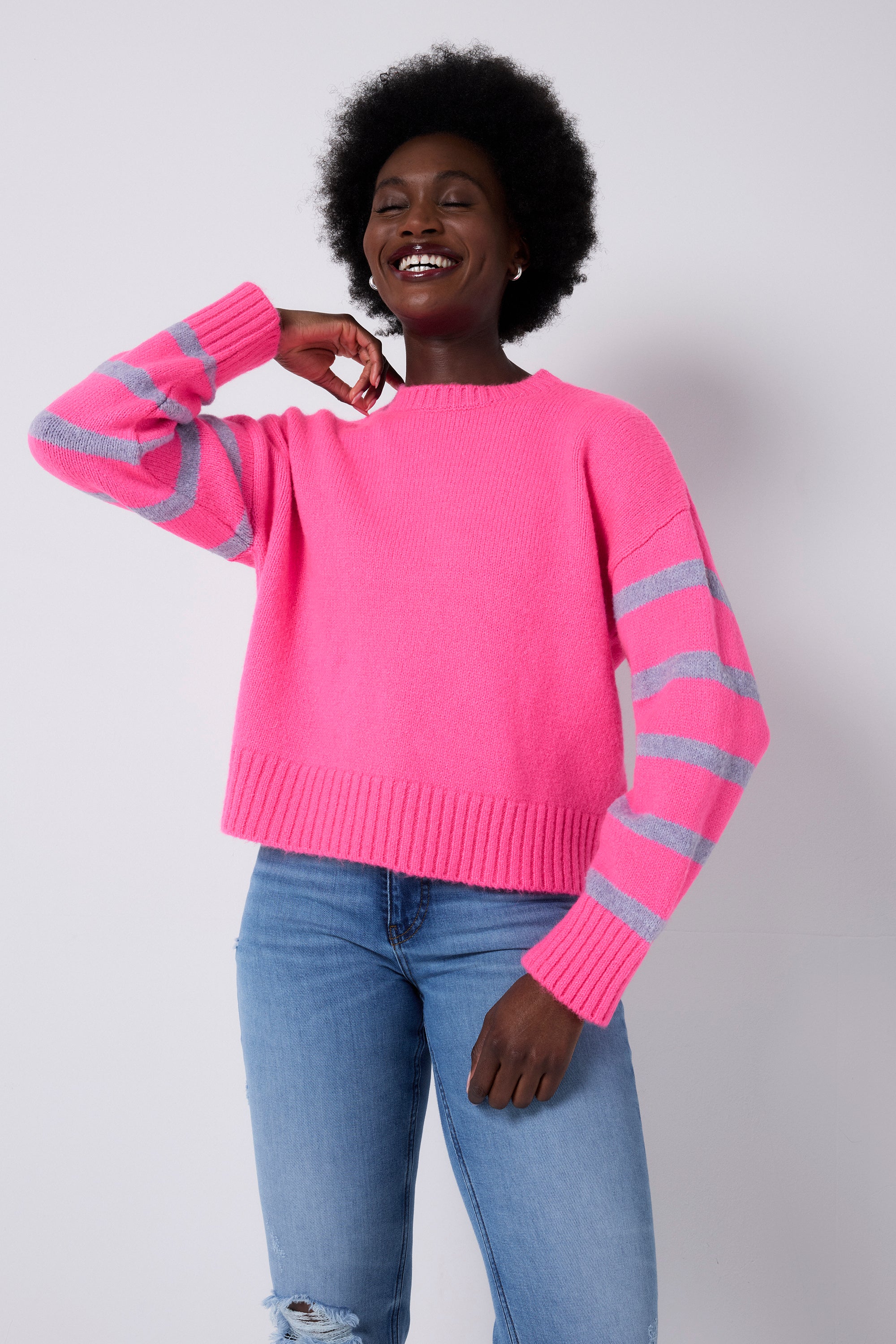 Scamp and Dude Pink and Lilac Stripe Knit Jumper | Model wearing a pair of blue jeans with a pink knit jumper featuring lilac stripes on the sleeves.