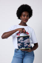 Scamp and Dude Navy Camo Lunch Bag | Model wearing a white t-shirt with red graphic print, paired with blue jeans. Holding a camo print lunch bag.