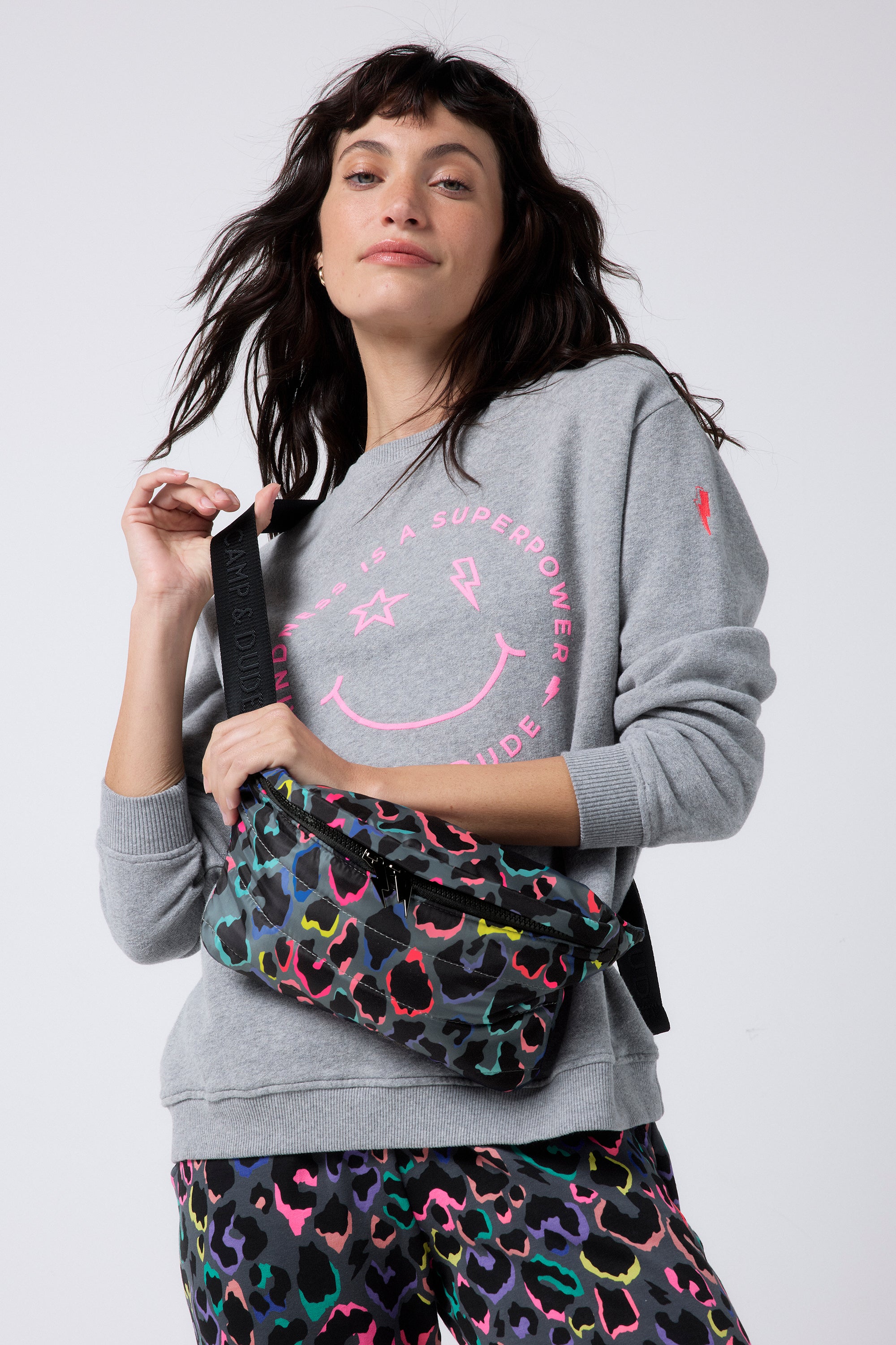 Scamp and Dude Grey with Rainbow Shadow Leopard Puffer Bum Bag | Model wearing a grey smiley face sweatshirt with rainbow leopard print joggers and a matching bum bag.