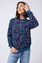 Scamp and Dude Teal with Rainbow Shadow Leopard Classic Sweatshirt | Model wearing a teal classic fit sweatshirt with rainbow shadow leopard print. Worn with blue distressed jeans.