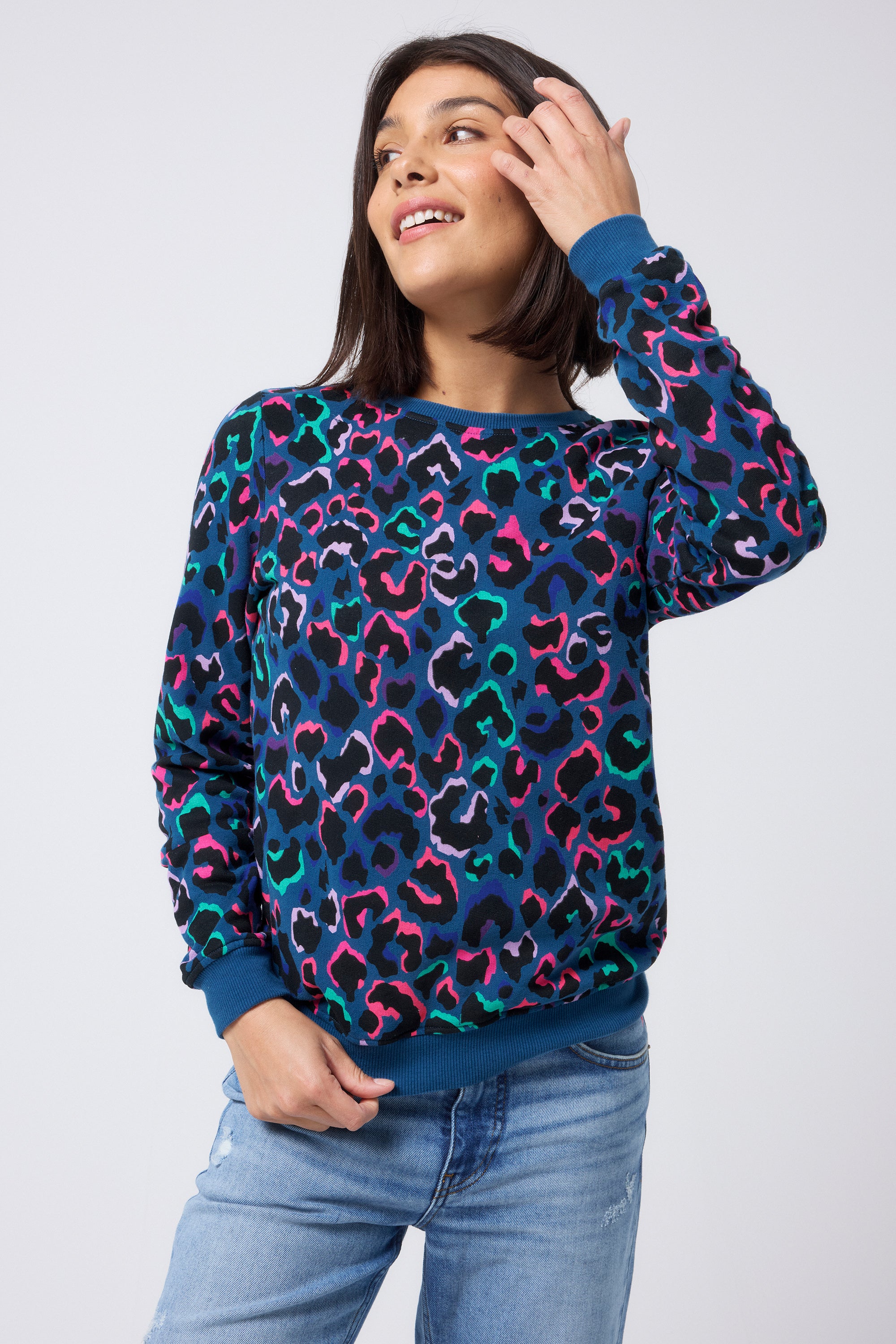 Scamp and Dude Teal with Rainbow Shadow Leopard Classic Sweatshirt | Model wearing a teal classic fit sweatshirt with rainbow shadow leopard print. Worn with blue distressed jeans.