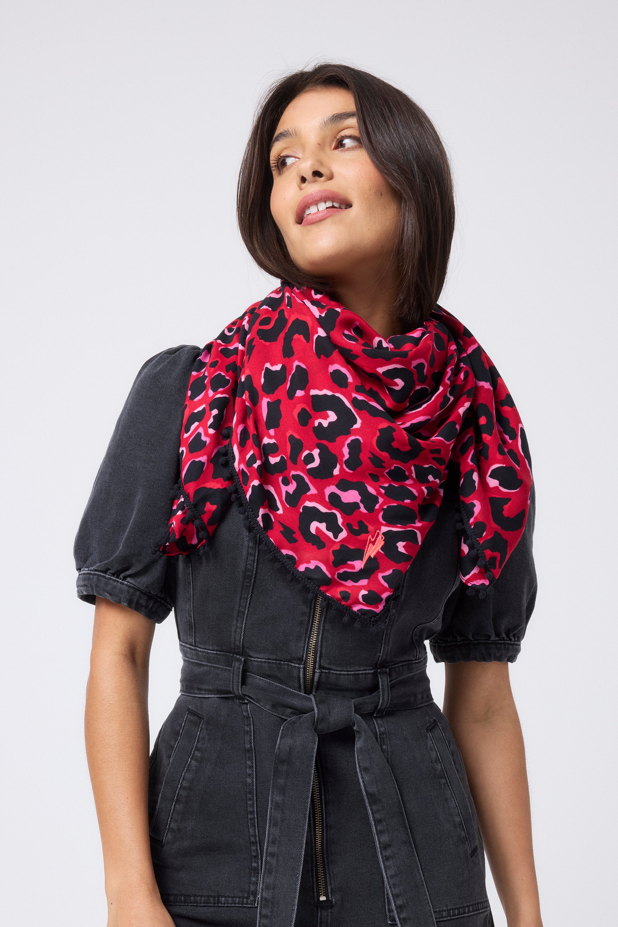 Scamp and Dude Red with Pink and Black Pop Leopard Charity Super Scarf | Model with short dark hair wearing a black denim playsuit and a red scarf with black leopard print around her neck.