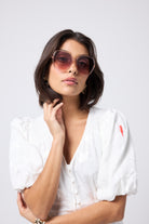 Scamp and Dude Margot Blush '70s Sunglasses | Model wearing a white puff sleeve tea dress with blush coloured sunglasses.