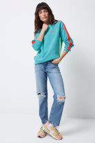 Scamp and Dude Bright Green with Coral Colourblock Relaxed Sweatshirt | Model wearing a green round neck sweatshirt with bright coral stripe down the sleeve. Paired with distressed jeans and trainers.