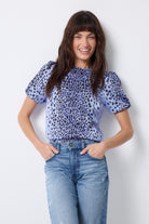 Scamp and Dude Blue with Black Wild Leopard Short Blouson Sleeve Top | Model with long dark hair wearing a blue round neck, puff sleeve top with a tie back detail. Worn with a pair of blue denim jeans.