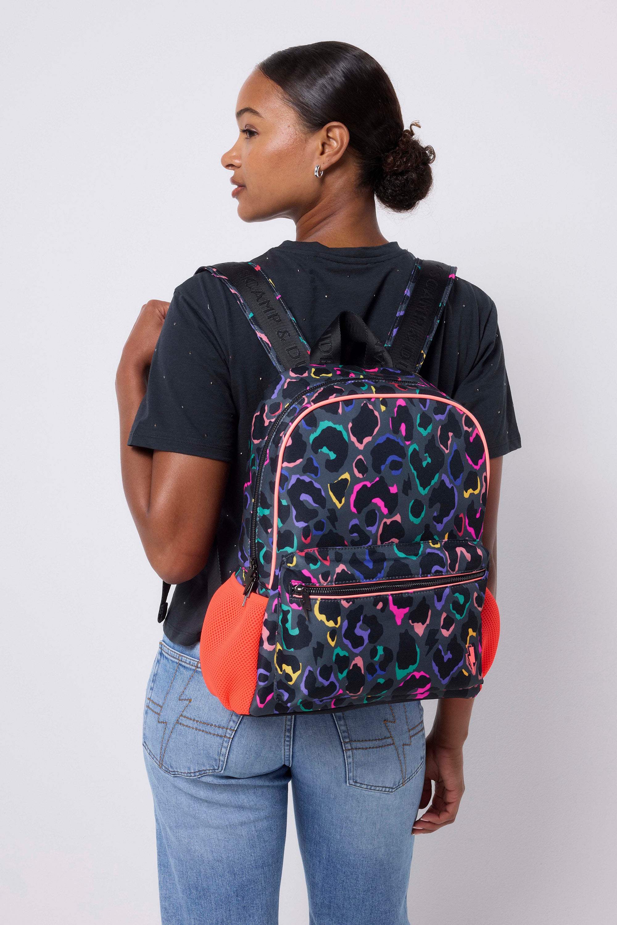 Scamp and Dude Grey with Rainbow Shadow Leopard Backpack | Model wearing a grey t shirt with blue jeans and a grey with rainbow leopard backpack.