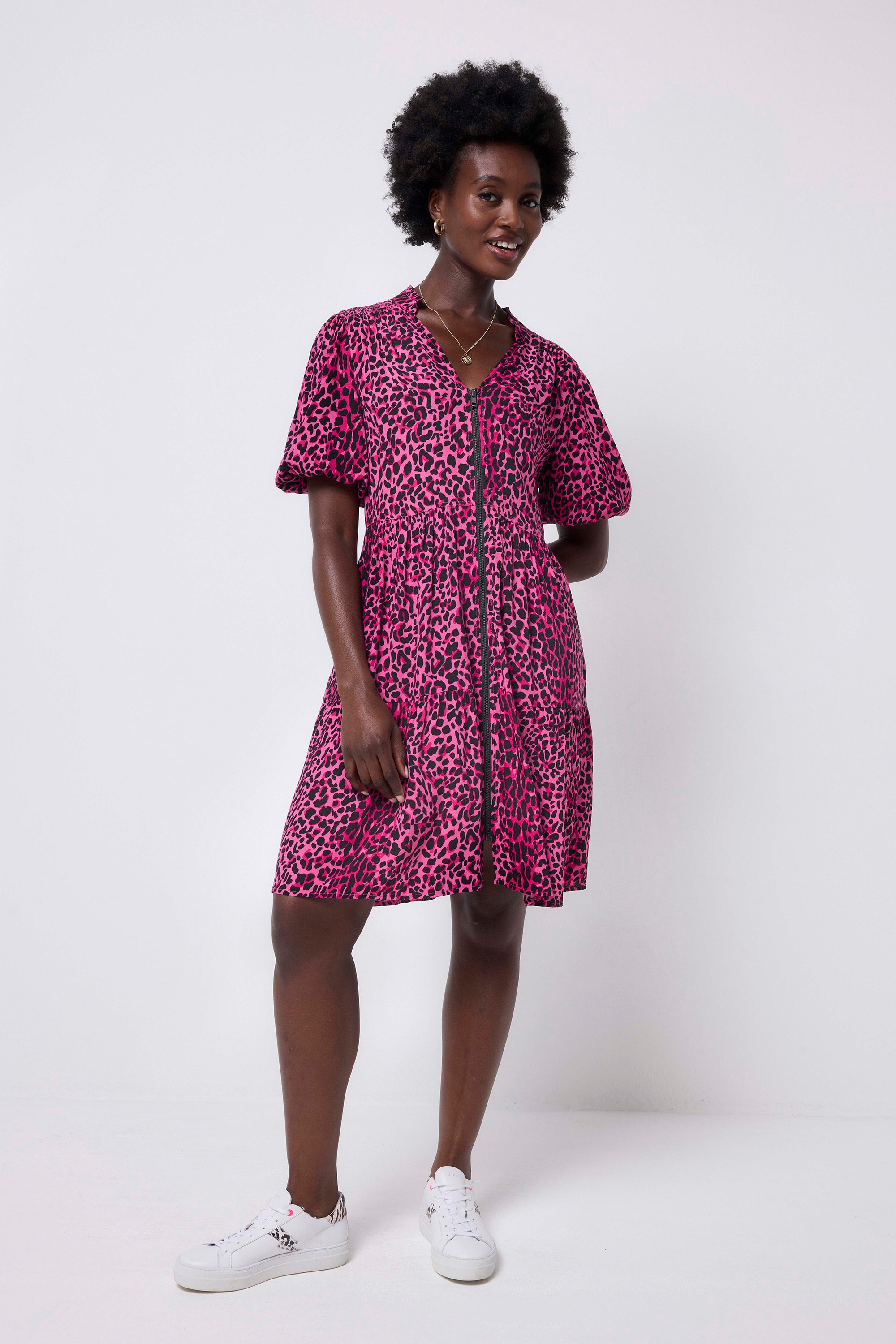 Scamp and Dude Pink with Black Wild Leopard Zip Detail Tiered Short Dress | Model wearing a pink puff sleeve dress in a wild leopard print with zip detail, paired with black tights and boots.
