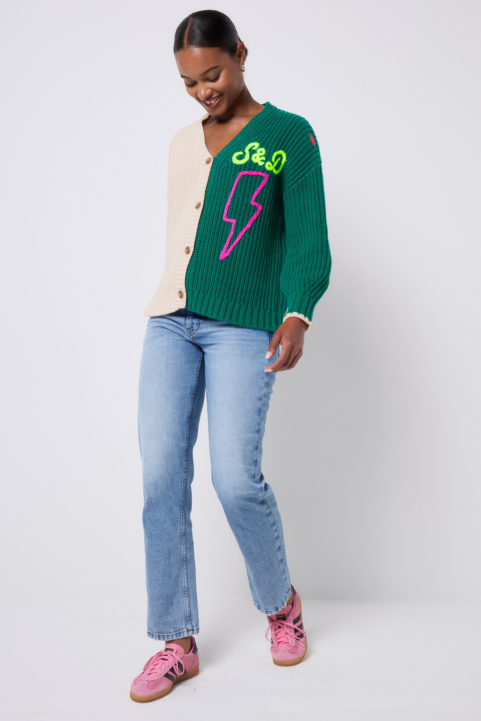 Scamp and Dude Cream and Green Colour Block Lofty Cardigan | Model wearing a cream and green split cardigan with neon S&D and bolt detail. Worn with pink trainers and blue jeans.