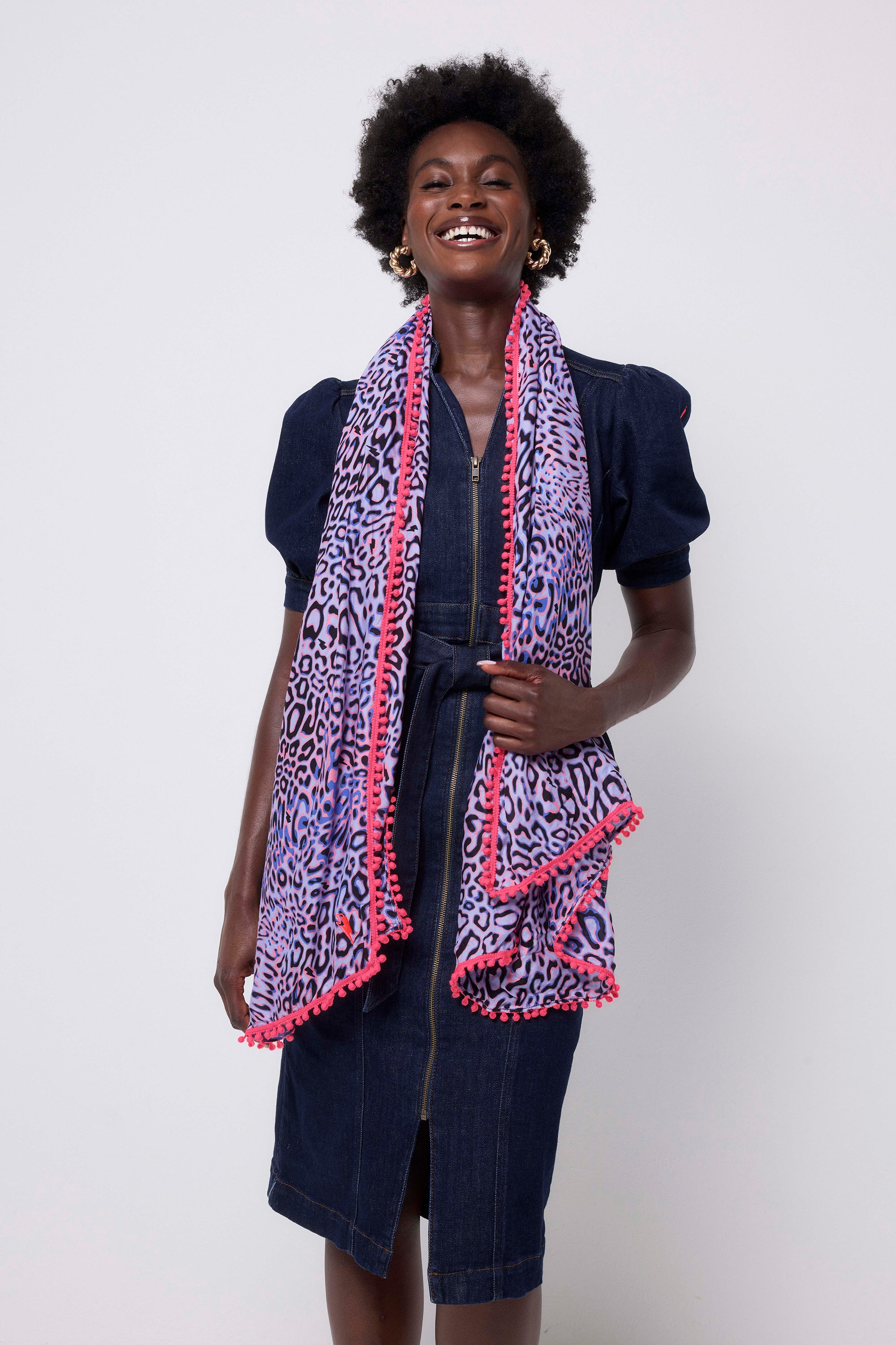 Scamp and Dude Lilac with Black and Pink Leopard Ray Super Scarf | Model wearing a dark blue denim dress with a lilac leopard ray print scarf with neon pink pom poms.