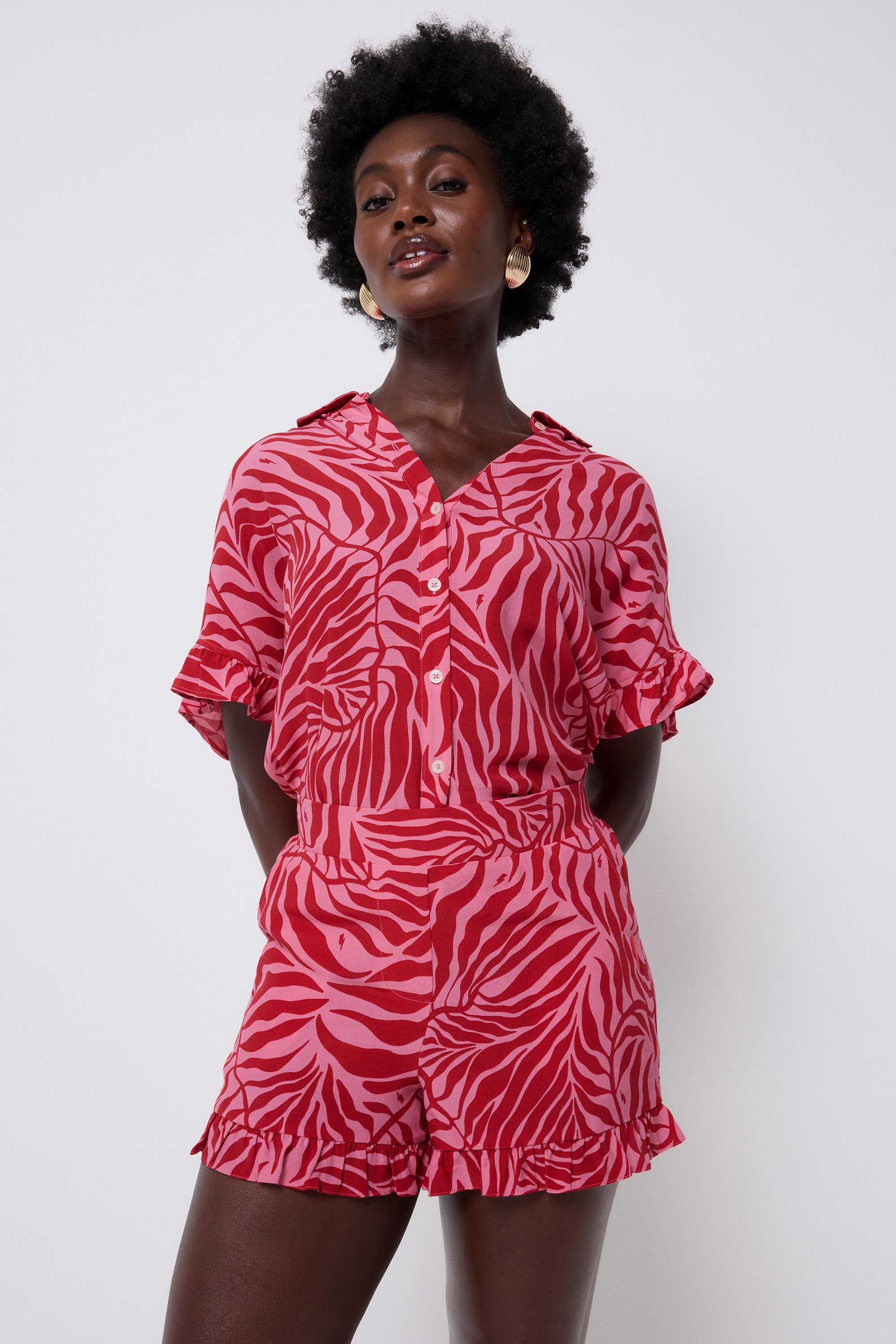 Scamp and Dude Pink with Red Palm Frill Hem Short | Model wearing a pink button front short sleeve shirt with red palm print. Worn with matching shorts.