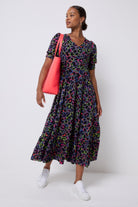 Scamp and Dude Grey with Rainbow Shadow Leopard Maxi Dress | Model wearing a grey maxi dress with rainbow leopard print. Worn with white trainers and holding a neon coral tote bag.