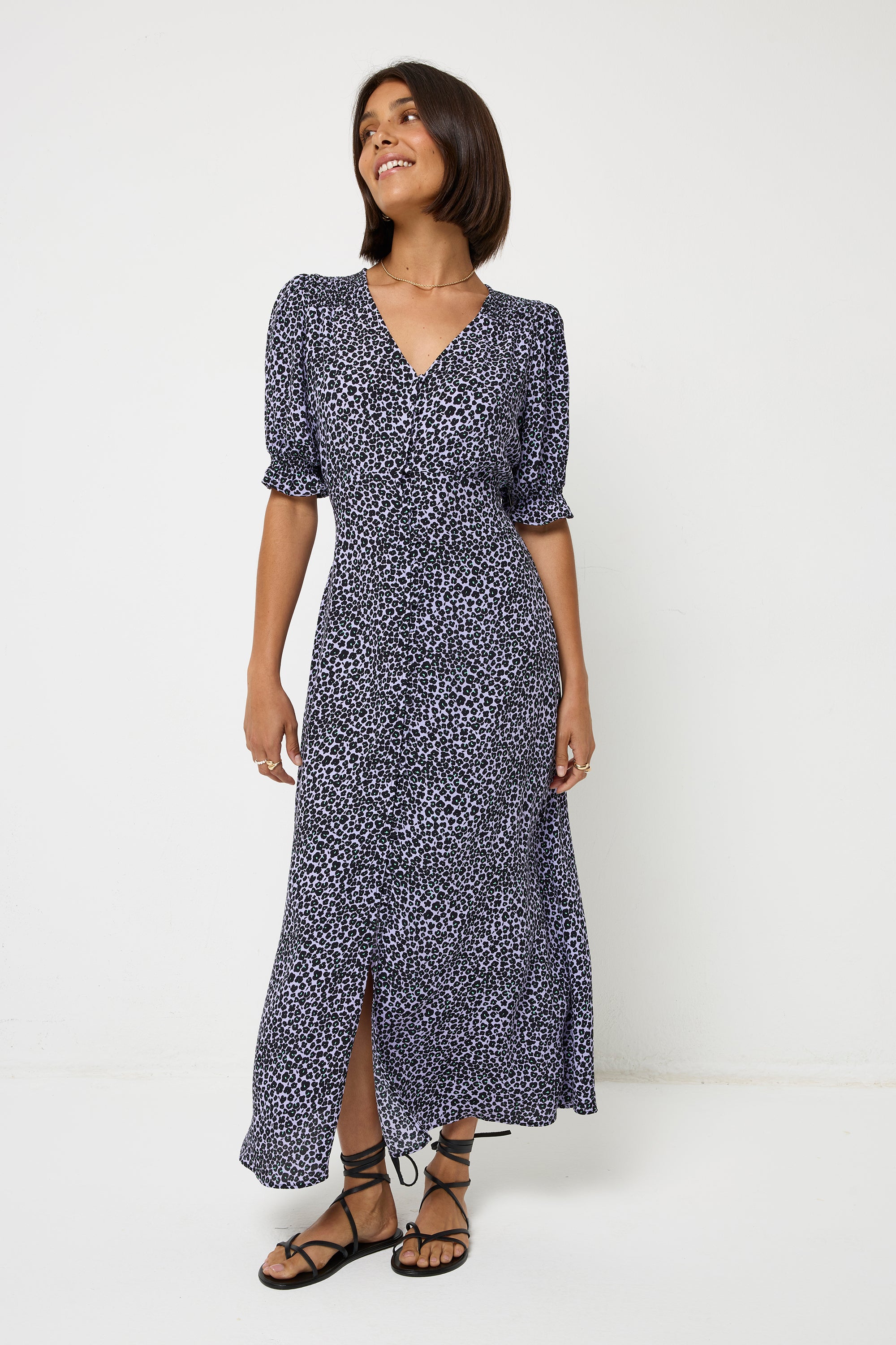 Scamp and Dude Lilac Mini Leopard Flute Sleeve Midi Tea Dress | Model with short dark hair wearing a lilac midi length tea dress with short flute sleeves and a button front detail. Worn with black strappy sandals and a gold necklace.