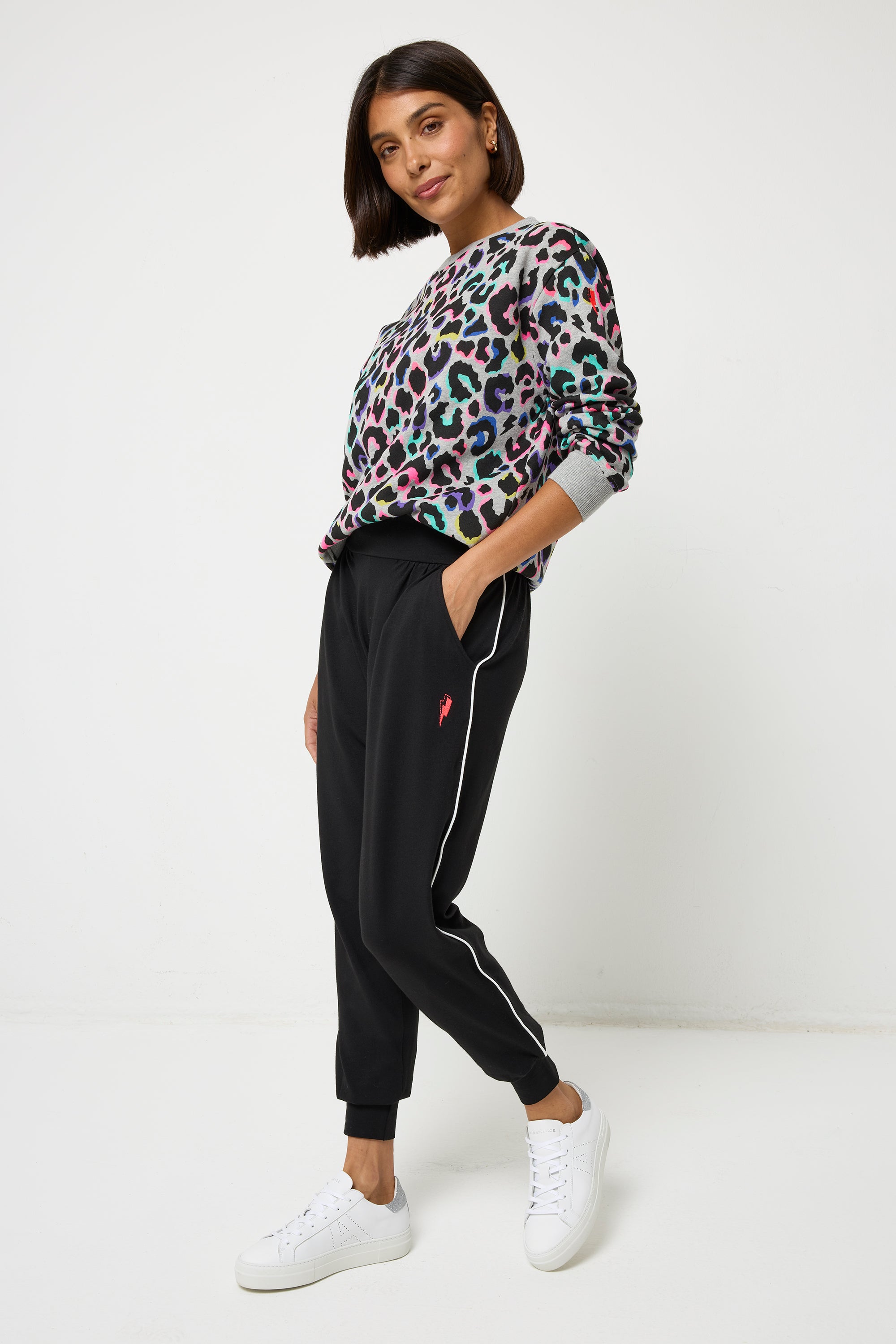 Scamp and Dude Black Slouch Jogger | Model wearing a crew neck grey rainbow leopard print sweatshirt with black joggers and white trainers.