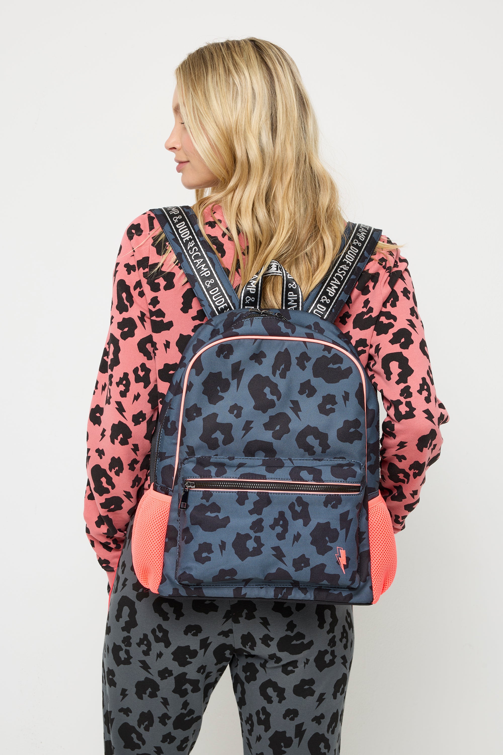 Scamp and Dude Grey with Black Leopard Backpack | Model wearing a coral sweatshirt and grey joggers with black leopard and lightning bolt print. Worn with a grey with black leopard and lightning bolt print backpack.