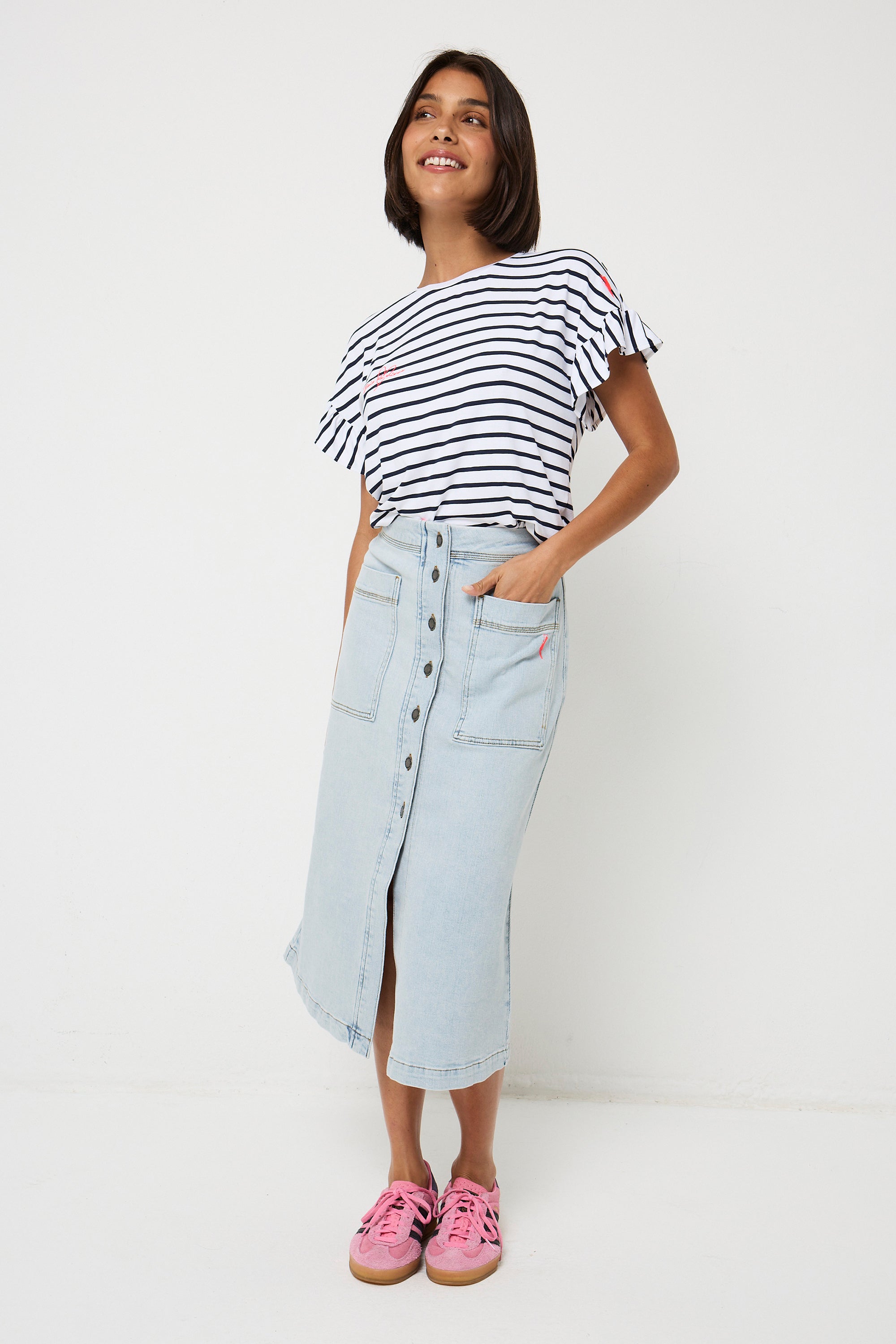 Scamp and Dude Pale Indigo Button Front A-Line Denim Midi Skirt | Model with short dark hair wearing a pale wash denim skirt with button front detail, paired with a stripe frill sleeve t shirt.