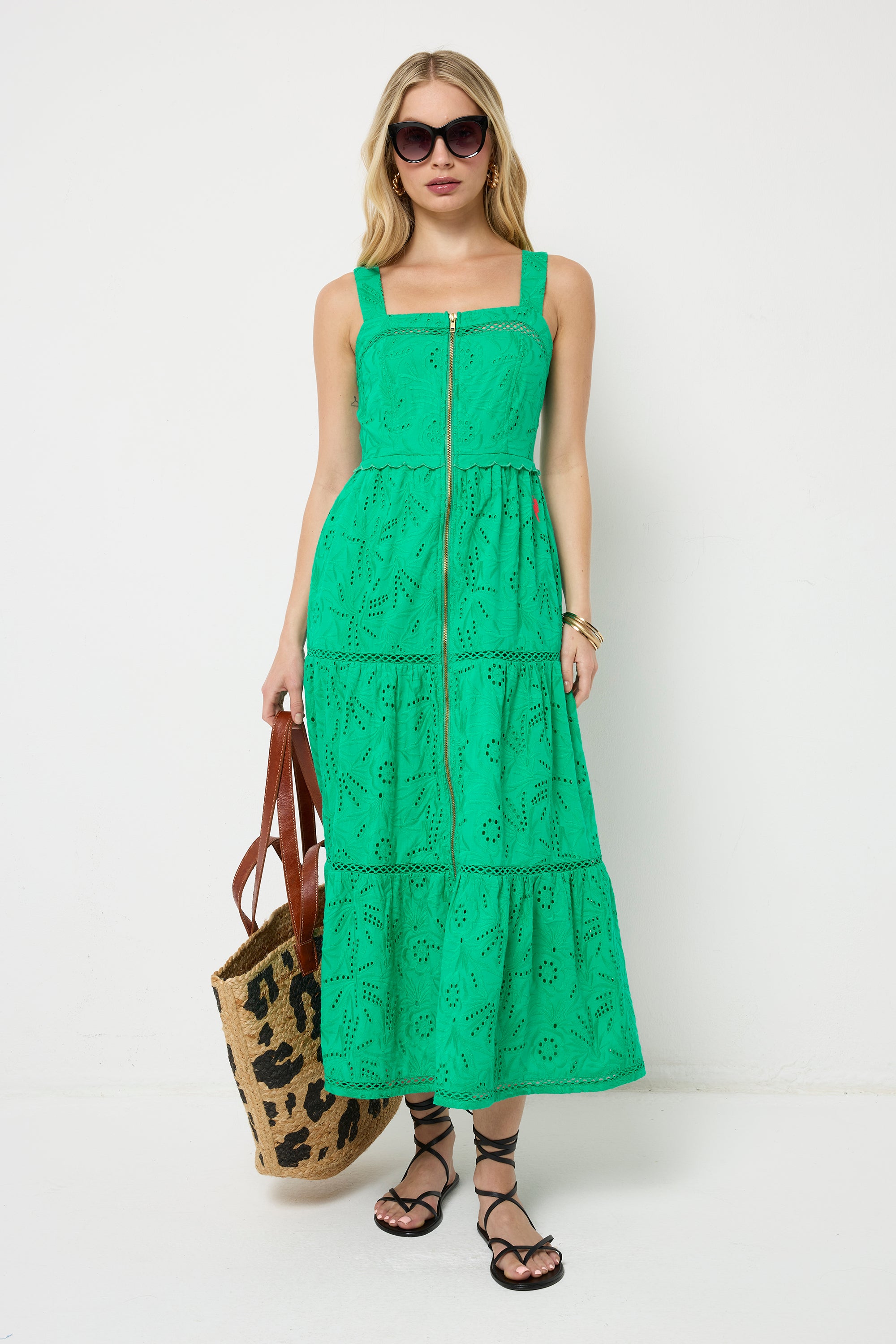 Scamp and Dude Green Broderie Zip Detail Midi Sundress | Model with blonde hair wearing a green broderie zip front midi dress with black sandals and sunglasses, holding a leopard print straw bag.