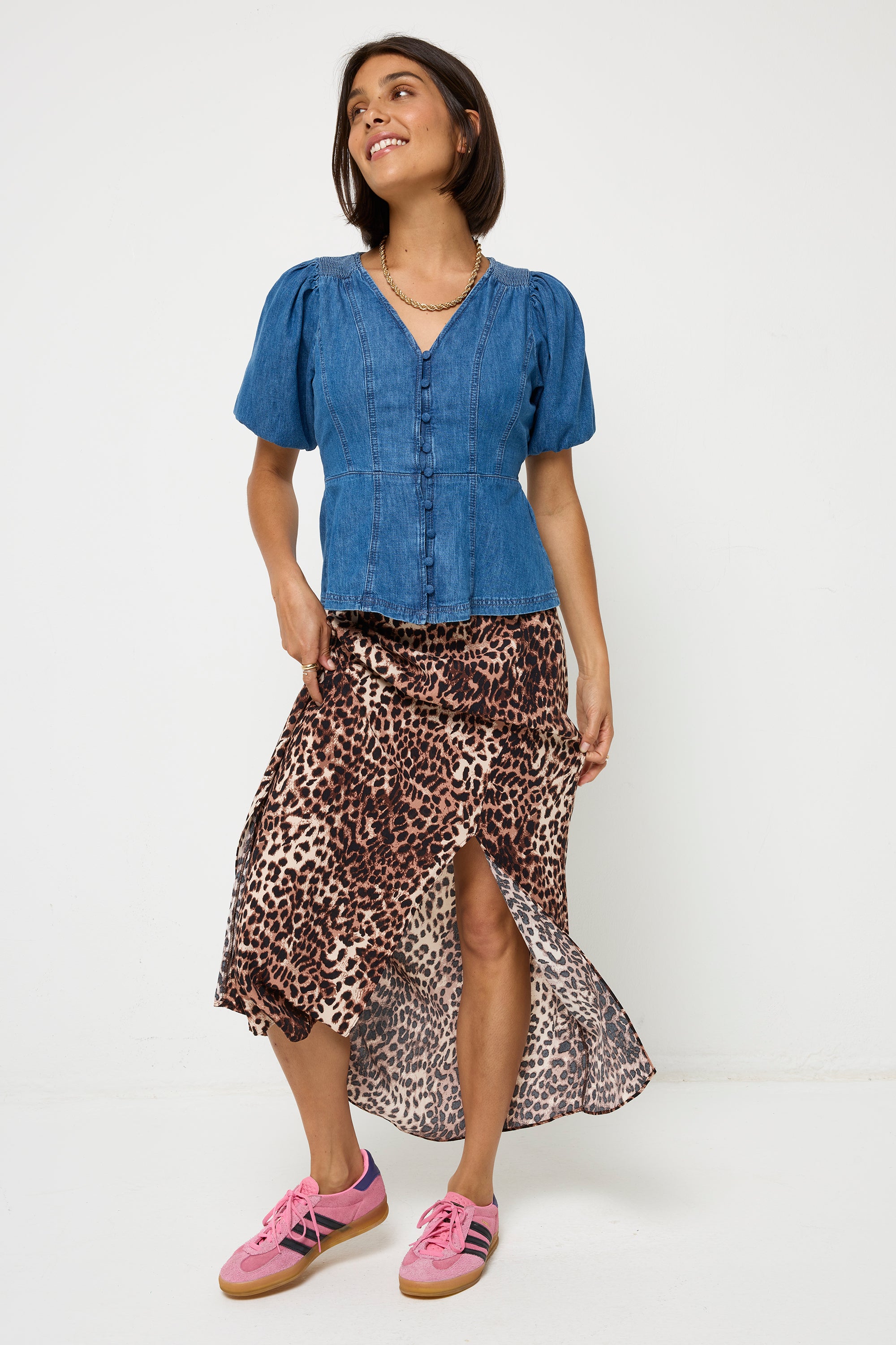 Scamp and Dude Indigo Button Through Denim Top | Model wearing a blue denim button through top with puff sleeves. Worn with a neutral and black cheetah print skirt and pink trainers.